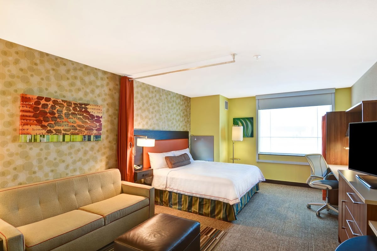 Ett hotellrum med en säng, en soffa, ett skrivbord, en tv och ett fönster.
