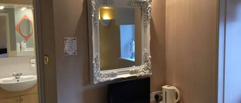 A bathroom with a large mirror, a sink, a toilet, and a small table with a remote control and a cup.