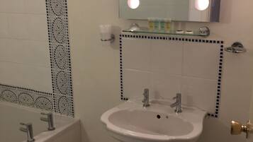 A bathroom with a white sink, two faucets, a mirror with lights, and a decorative tile border.