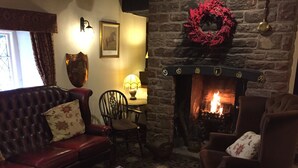 A cozy living room with a stone fireplace, a red leather sofa, a wooden coffee table with books, and a patterned carpet. - String of Horses (Brampton)