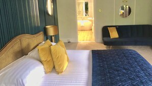 A bedroom with a bed, a blue sofa, a mirror, and a lamp. - String of Horses (Brampton)