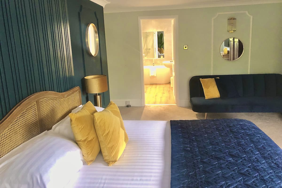 Ett sovrum med en säng, en blå soffa, en spegel och en lampa.