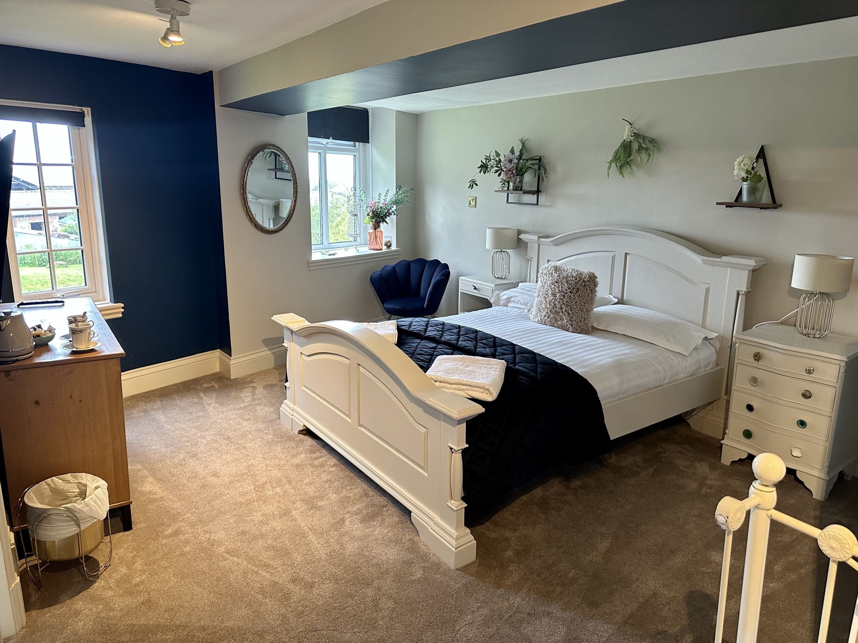 A bedroom with a bed, bedside tables, a chair, a window, a mirror, and a small desk with a lamp.