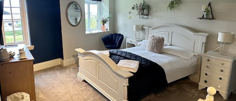 A bedroom with a bed, bedside tables, a chair, a window, a mirror, and a small desk with a lamp.