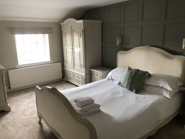 A bedroom with a large bed, a wardrobe, a nightstand, and a window with blinds.