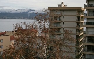 Un edificio de varios pisos con balcones que dan a un cuerpo de agua y montañas al fondo.