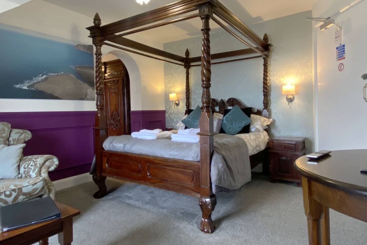A four-poster bed with a canopy, a bedside table, a nightstand, and a desk with a chair.