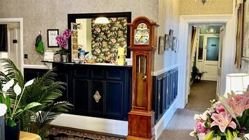 Un salon spacieux, agrémenté d’un buffet en bois foncé, d’un grand miroir, d’une horloge comtoise et d’un lustre.