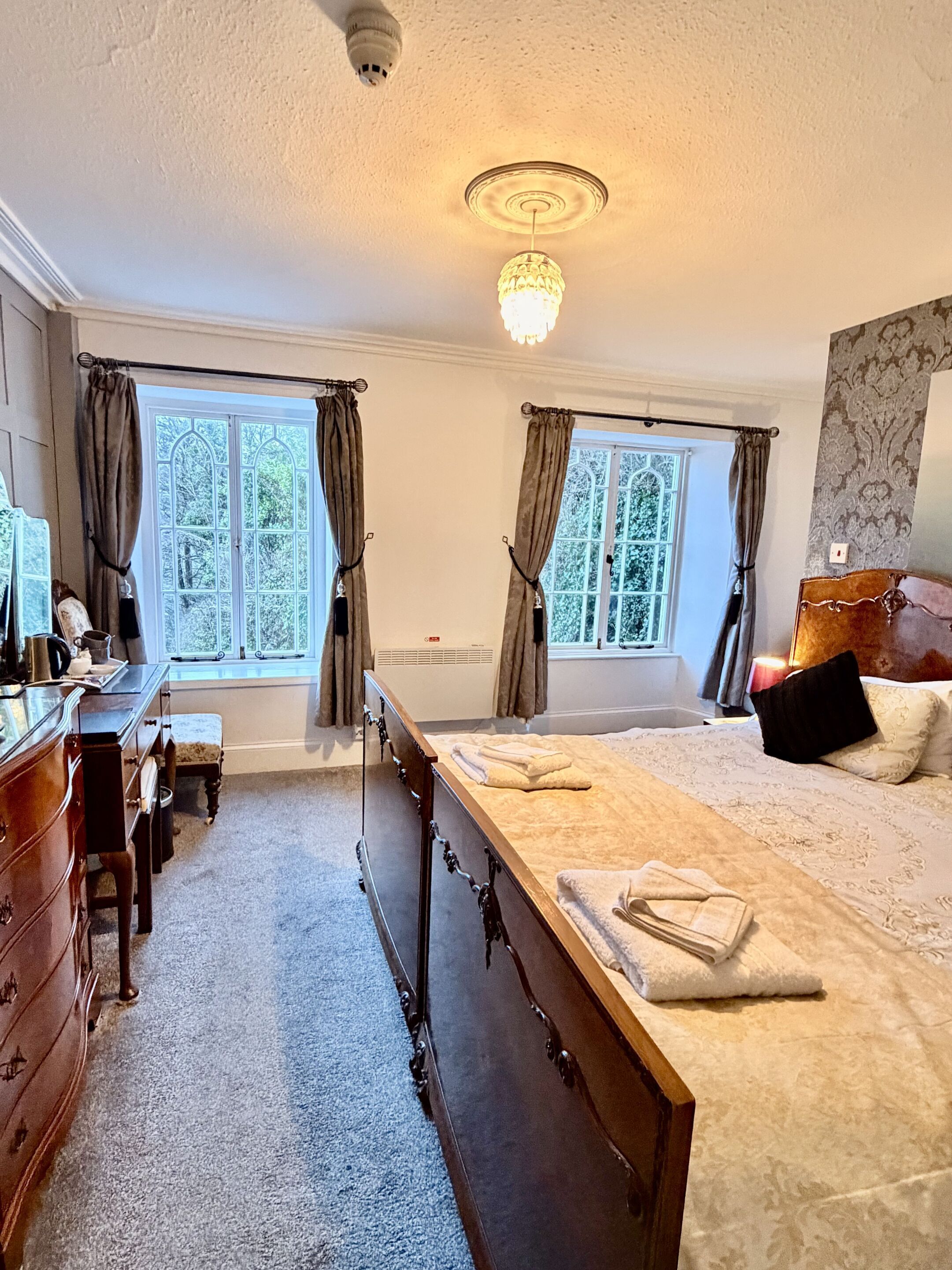 A bedroom with a large bed, a wooden dresser, a desk with a chair, and a window with curtains.
