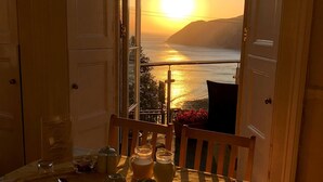 Mesa de comedor lista para dos, con vista al atardecer sobre el agua, puertas abiertas y un atril para el menú.