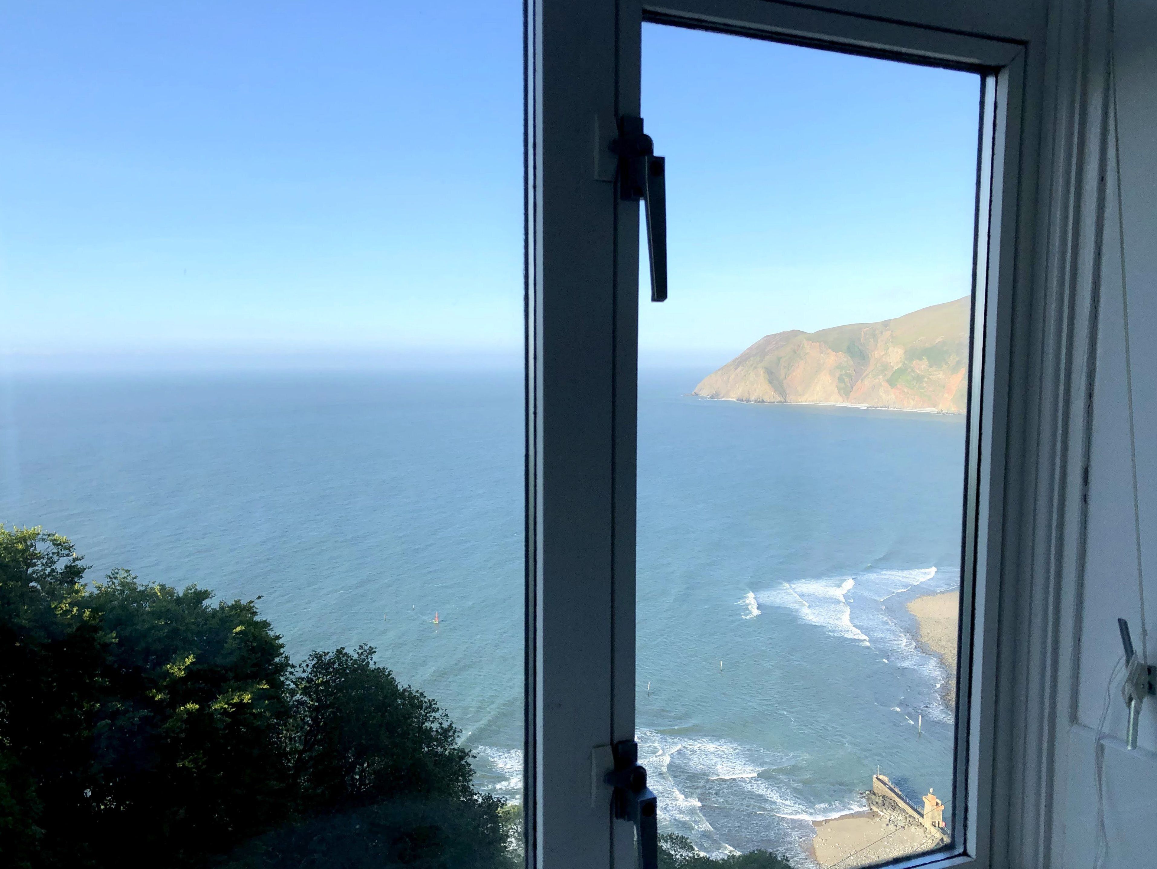 Uitzicht op de oceaan vanuit een raam, met een heldere lucht en land in de verte.