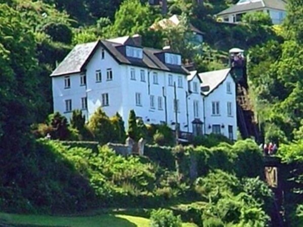 A large white building with multiple windows, surrounded by lush greenery. - The North Cliff Hotel (Lynton)