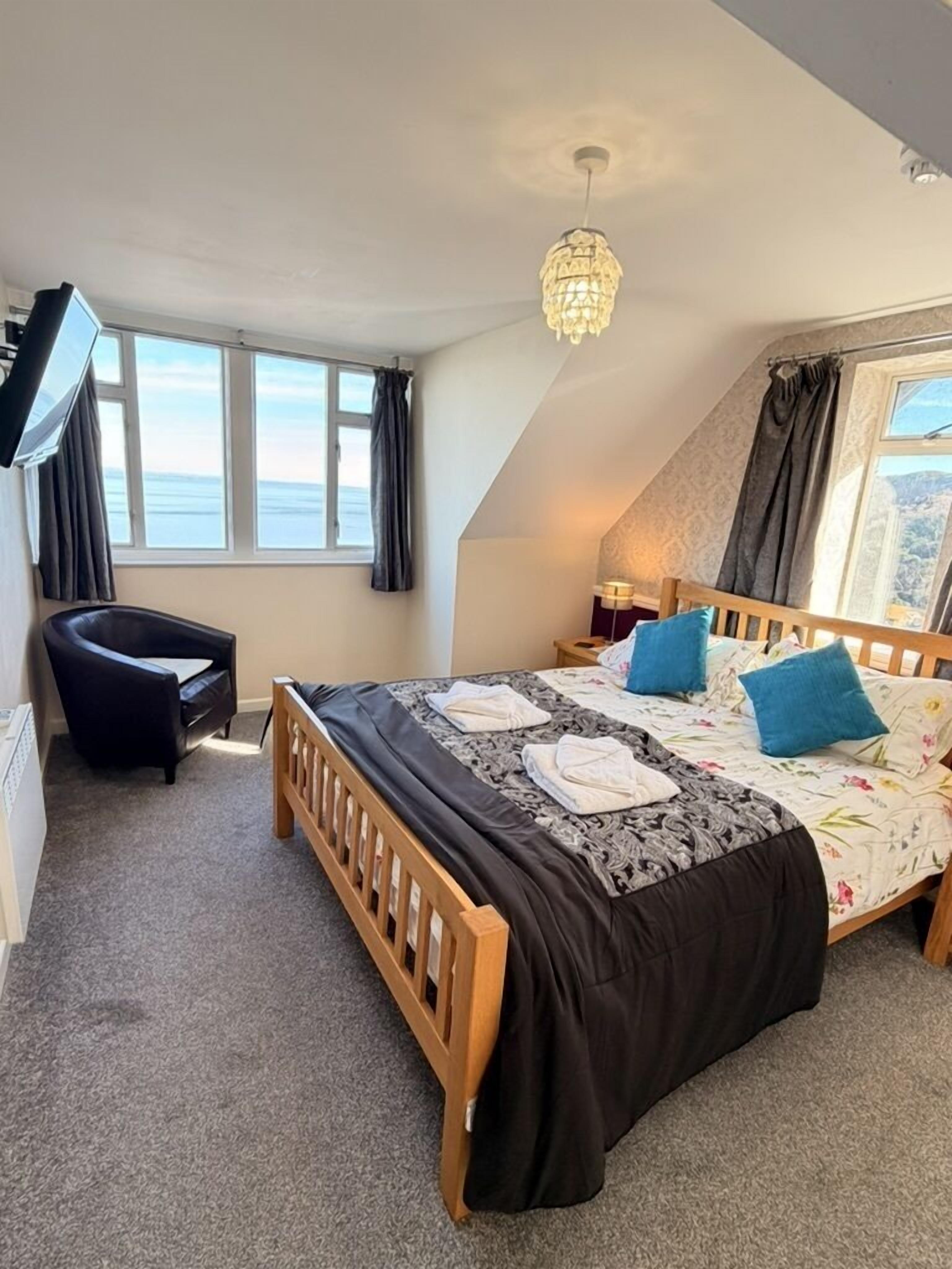 A bedroom with a bed, a chair, a desk, and a window with a view.