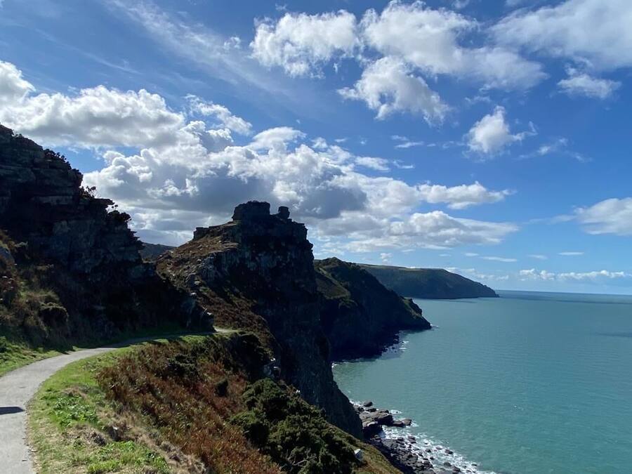 Uma estrada costeira com falésias rochosas e vista clara do mar.