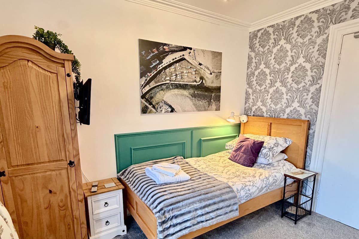 A bedroom with a wooden bed, a green headboard, a mounted TV, a ceiling light, and a wall-mounted security camera.
