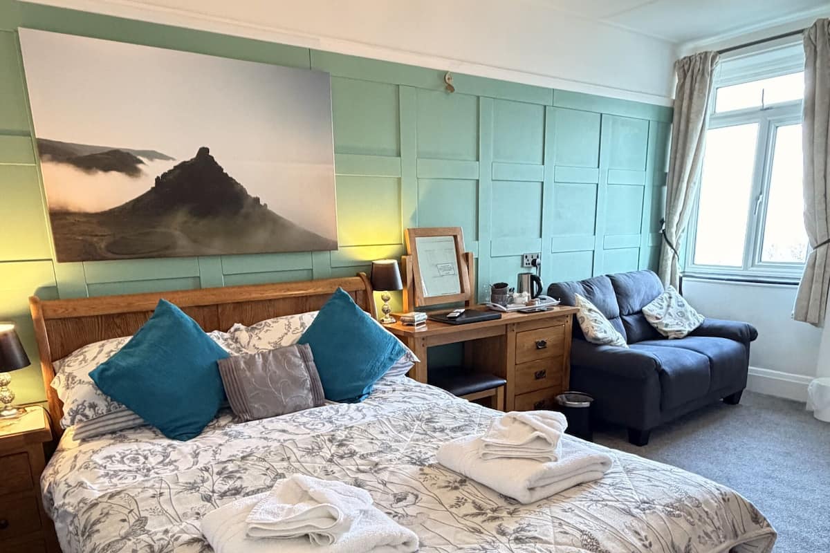 A bedroom with a large bed, a desk, a chair, and a painting on the wall.
