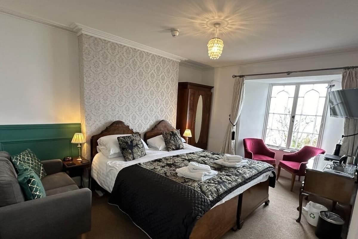 A hotel room with a large bed, a desk, a chair, and a window with curtains.