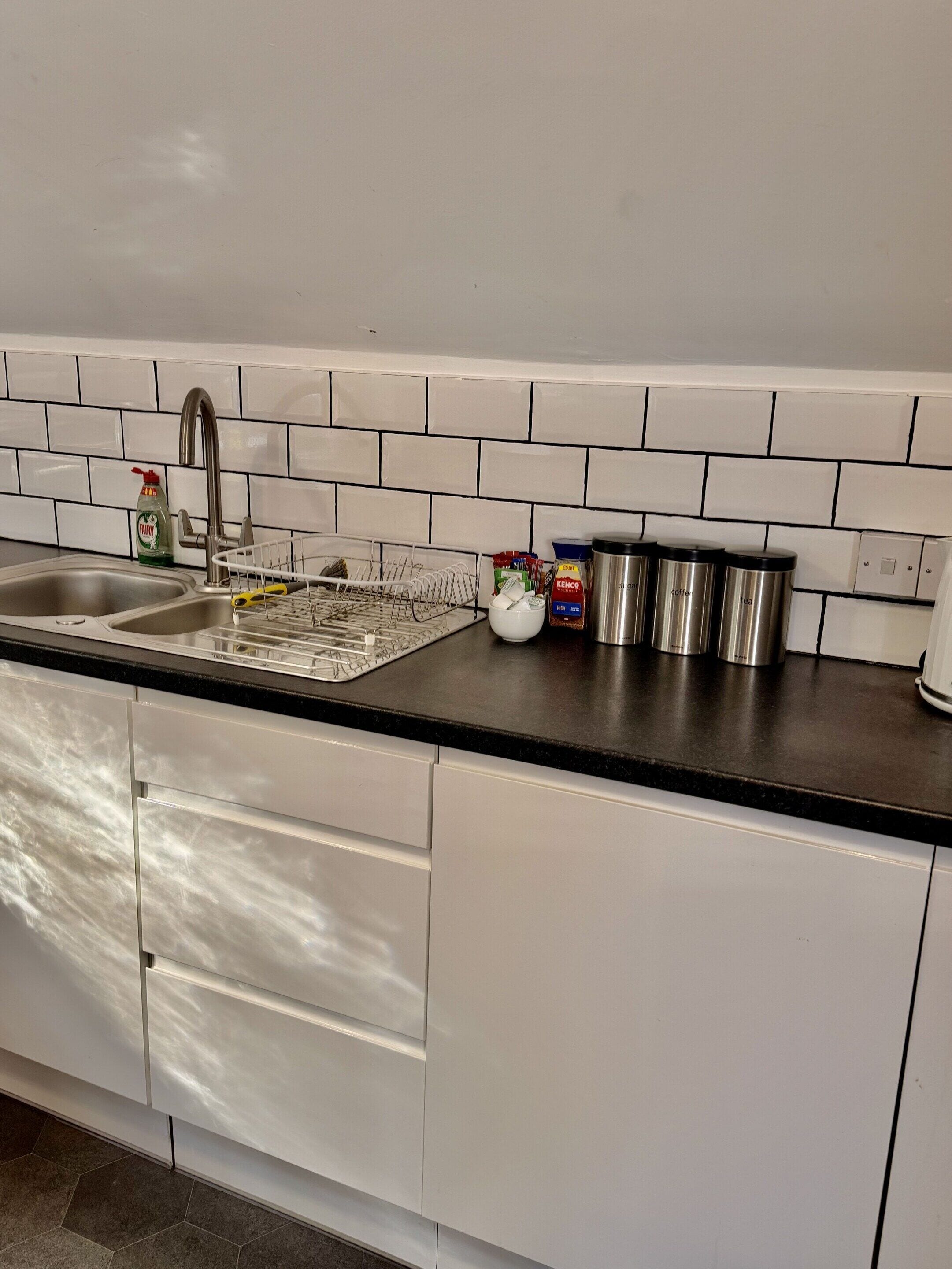 A kitchen with white cabinets, a black countertop, a stainless steel sink, and a dish rack.