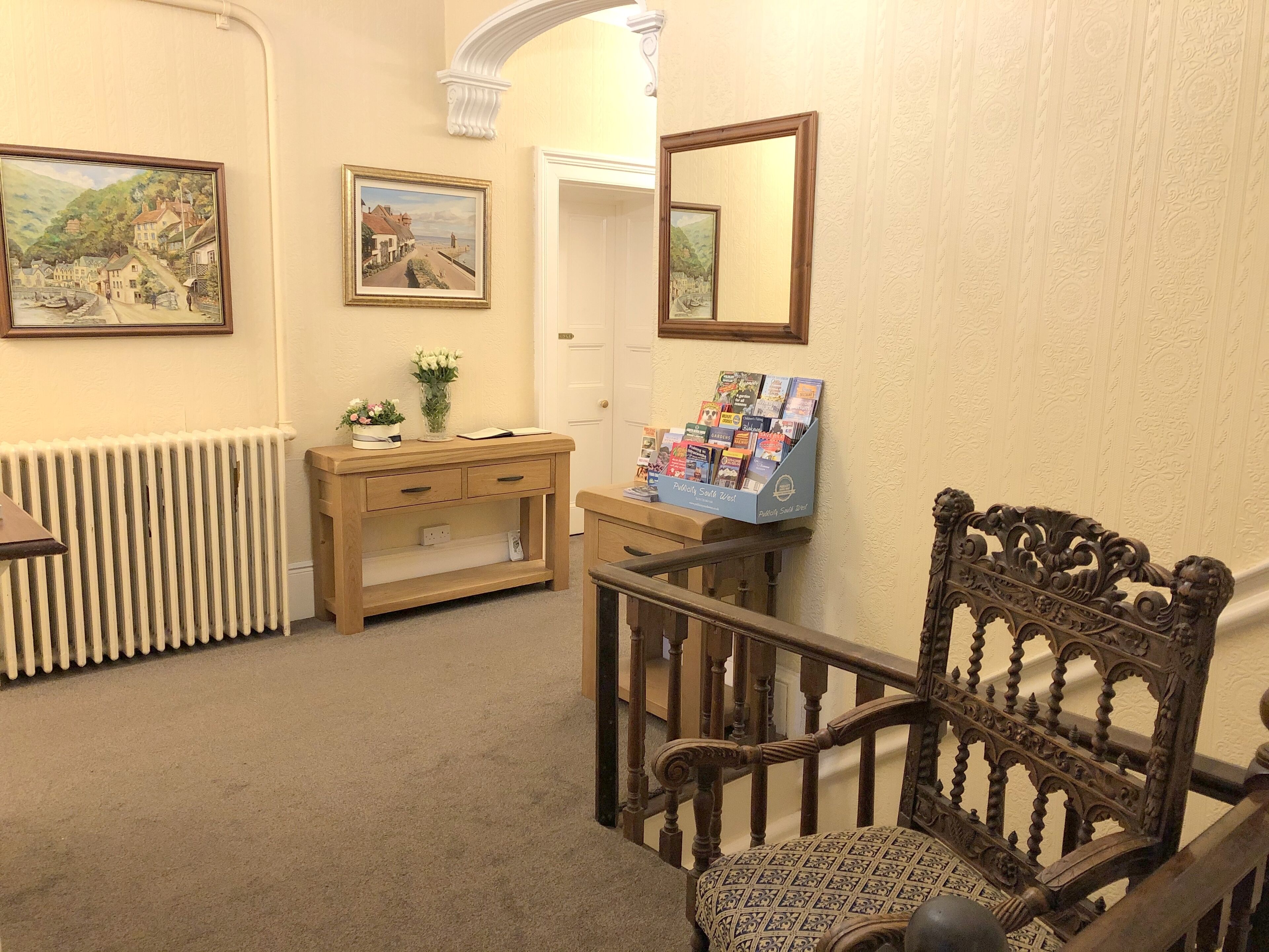 A room with a wooden desk, a chair, a radiator, and two framed paintings on the wall.