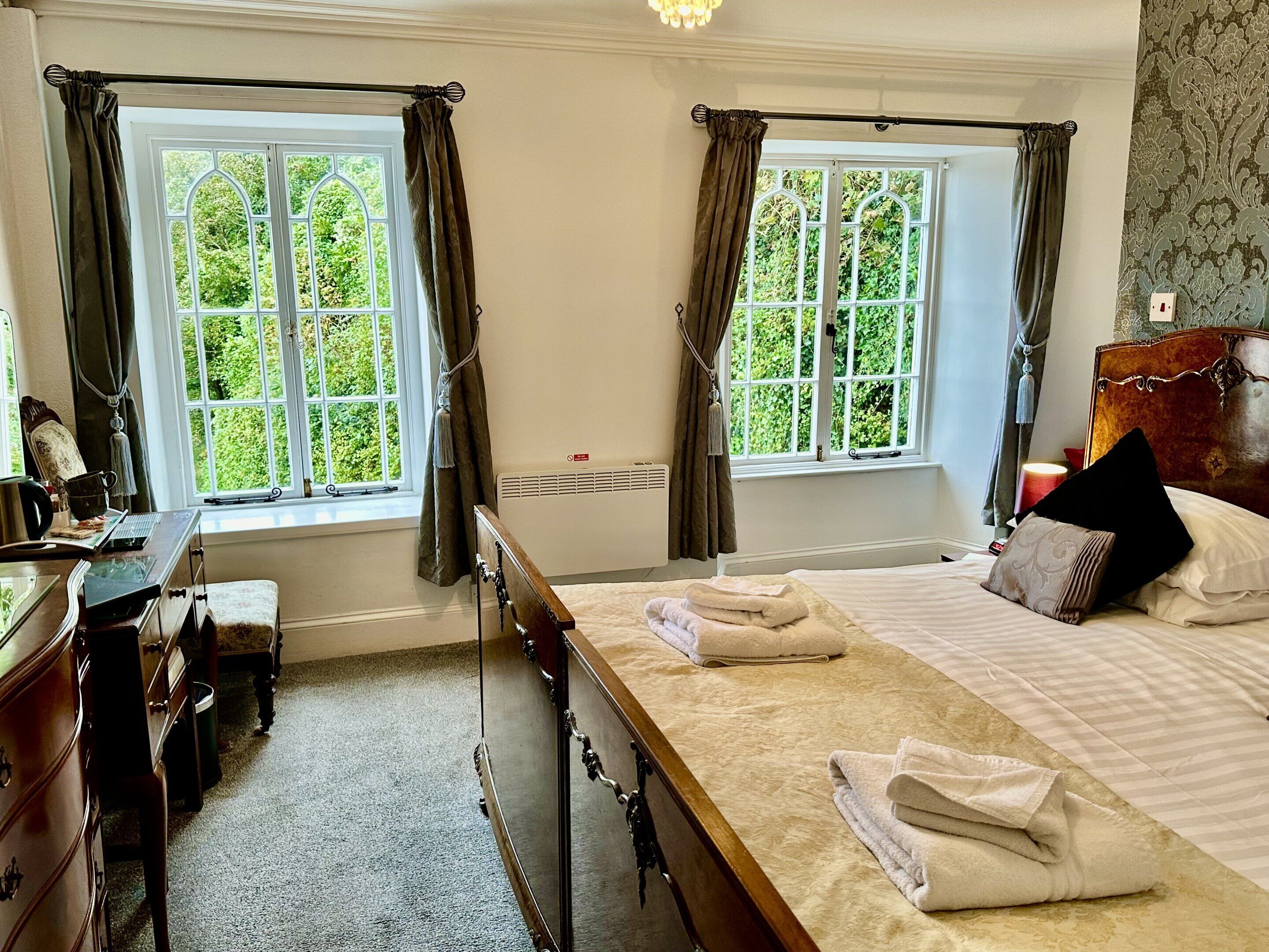 A bedroom with two windows, a bed with pillows, a bedside table, and a dresser.