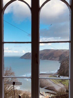 A view through a window with a view of the sea, hills, and a small village. - The North Cliff Hotel (Lynton)