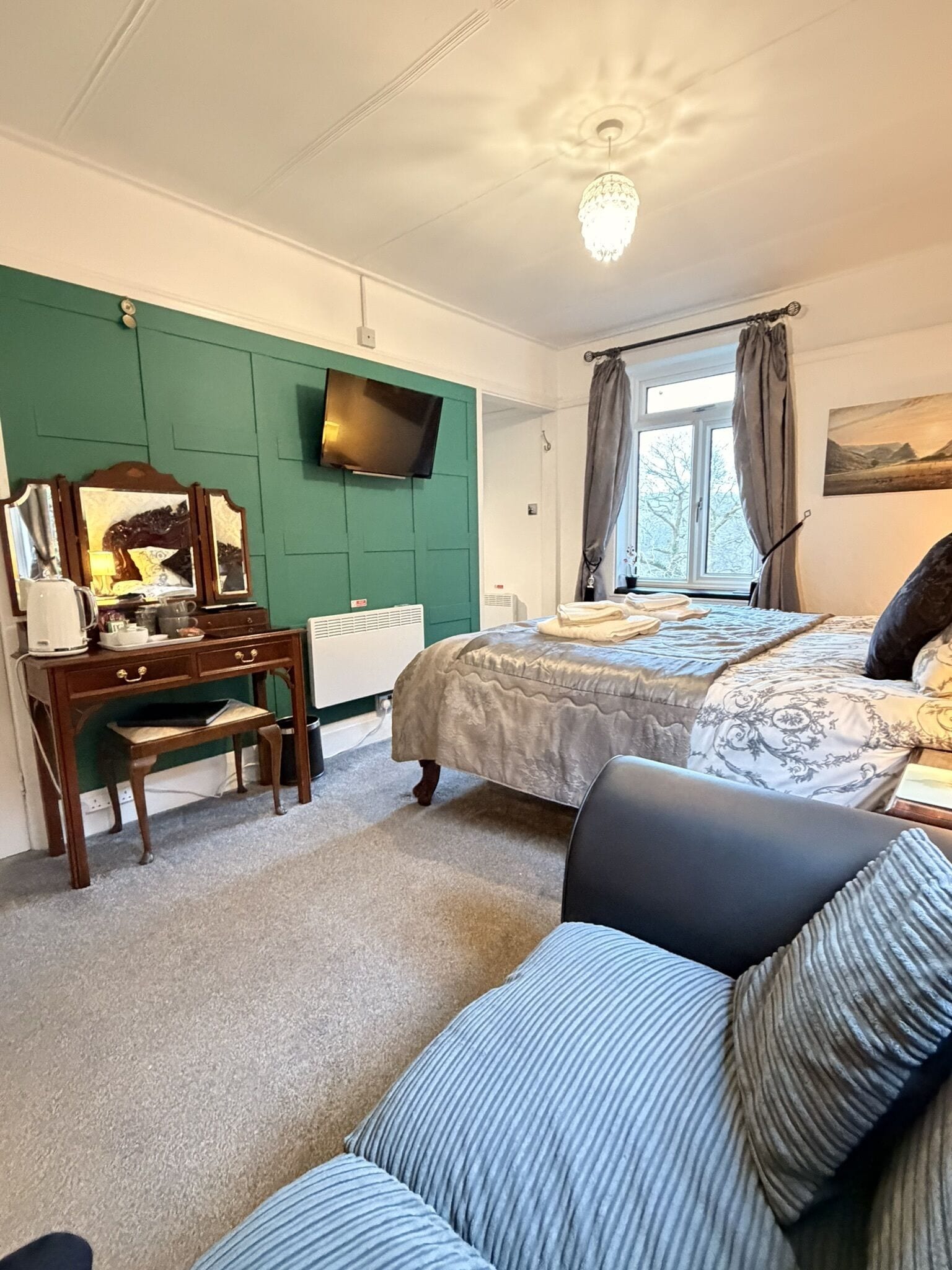 A bedroom with a bed, a desk, a chair, a television, and a window with curtains.