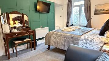 Un dormitorio con cama, escritorio, silla, televisor y ventana con cortinas.
