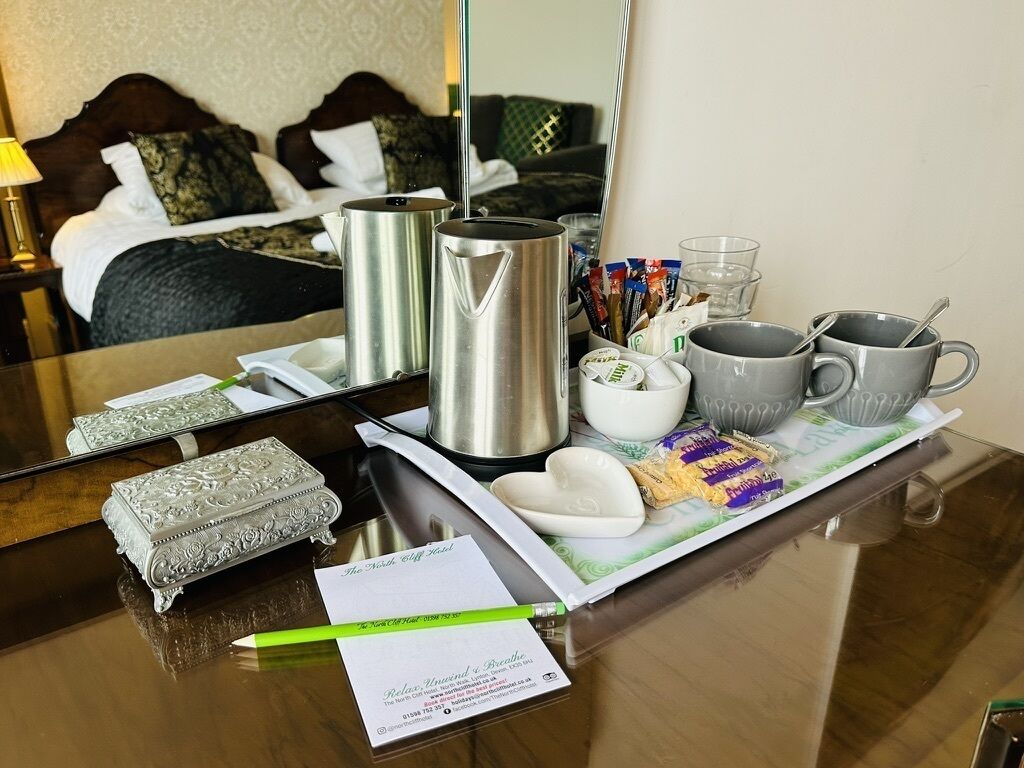 A hotel room with a neatly arranged breakfast tray including a coffee pot, mugs, and a small decorative box.
