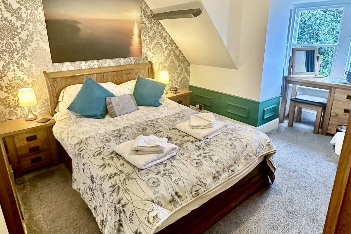 A bedroom with a large bed, a nightstand, a desk, and a chandelier.