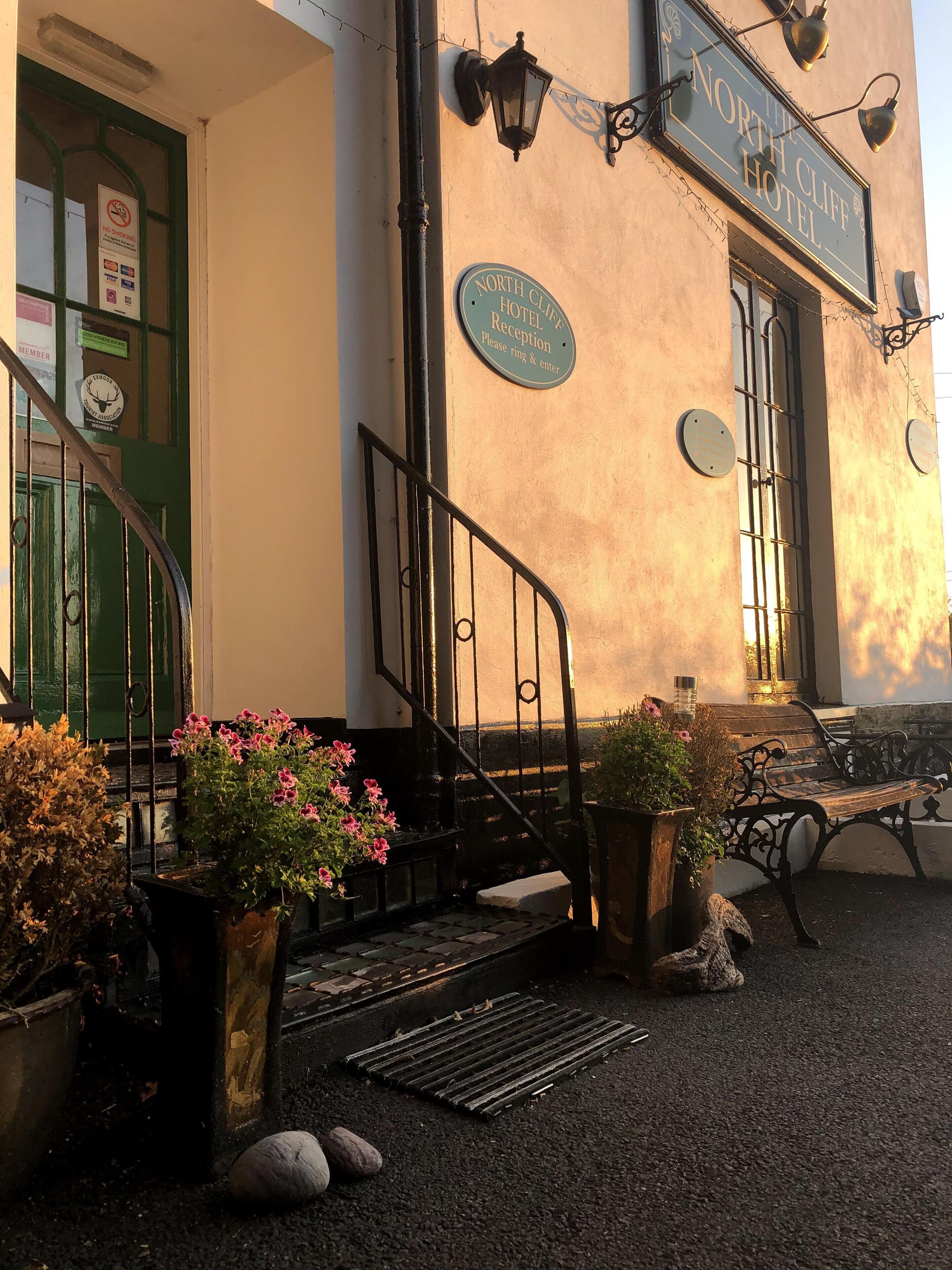 The exterior of The North Cliff Hotel with a reception sign, a staircase, and potted plants.