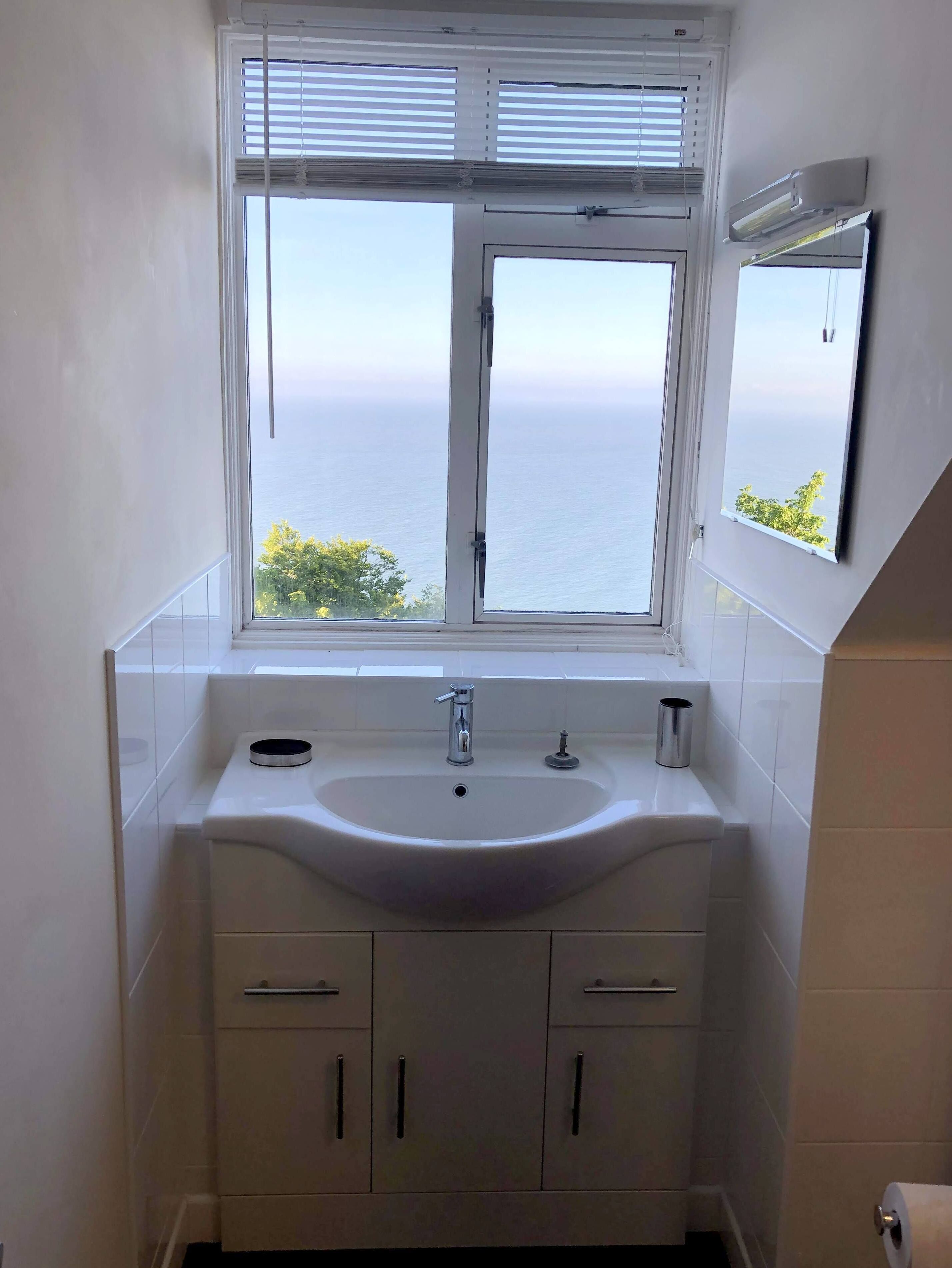 A bathroom with a white sink, two cabinets, and a window with blinds.