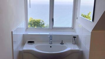 A bathroom with a white sink, two cabinets, and a window with blinds.