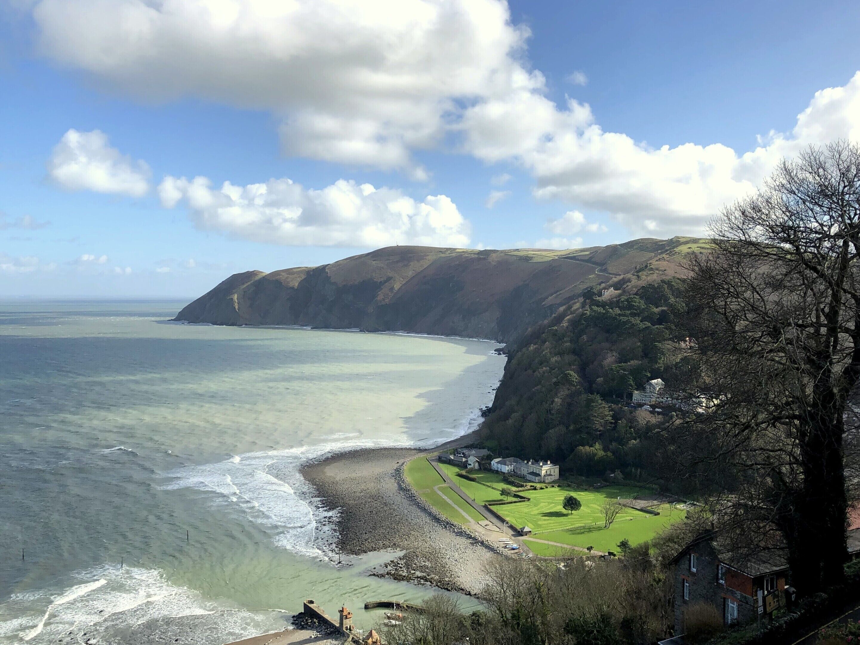 A coastal landscape with a beach, cliffs, and a house with a lawn.