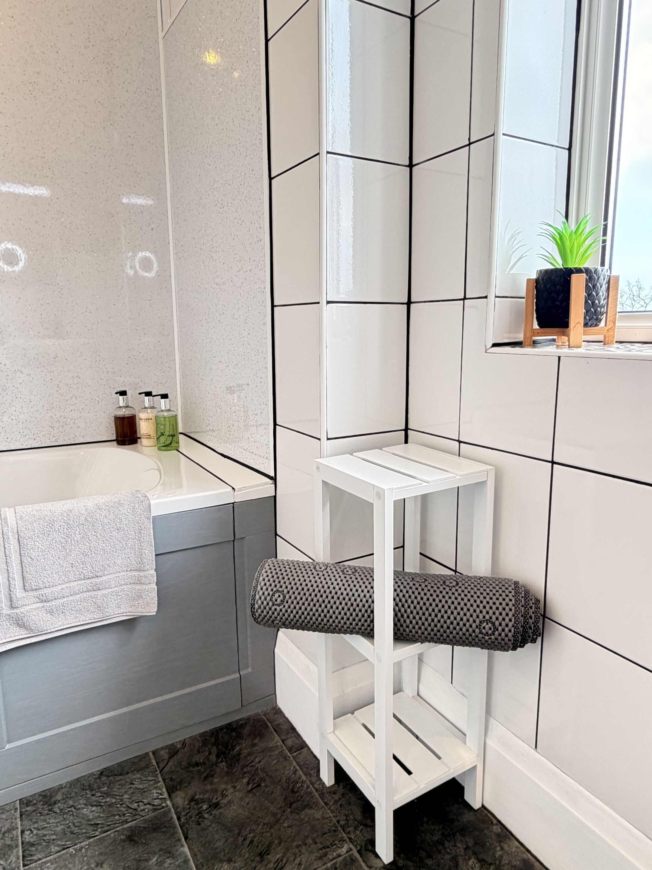 A modern bathroom with a bathtub, a small white table, a towel, and toiletries on the counter.