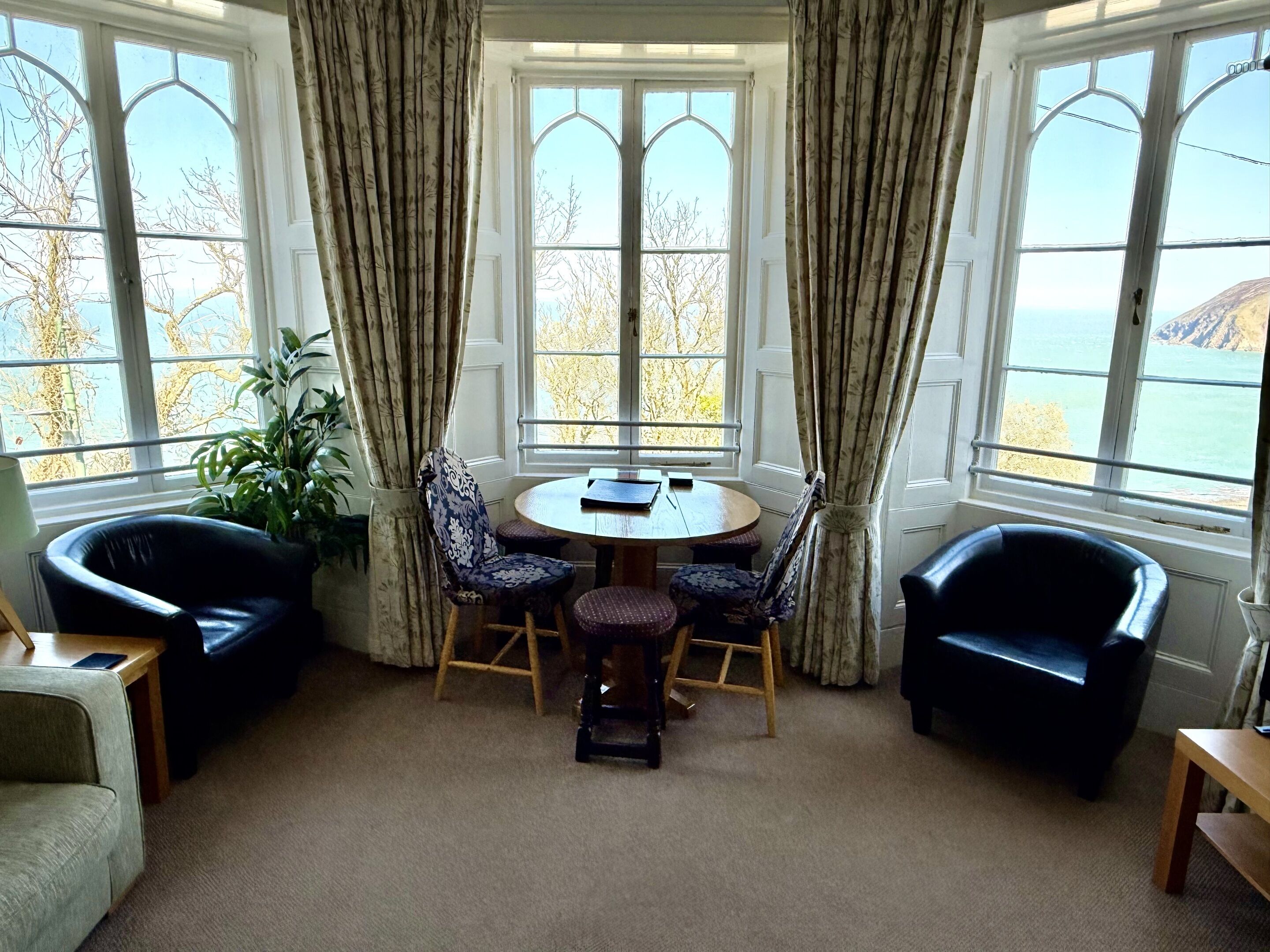 A room with a round table, four chairs, and a view of the sea through large windows.