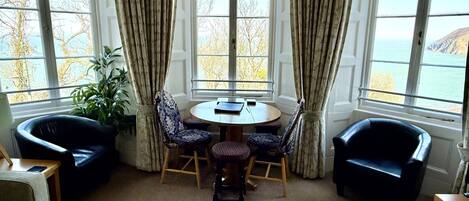 A room with a round table, four chairs, and a view of the sea through large windows.