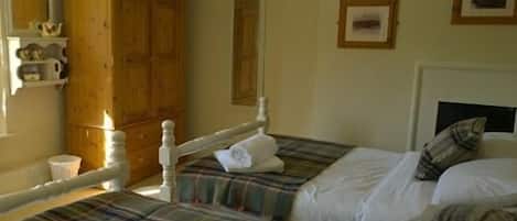 A bedroom with two beds, a wooden wardrobe, a mirror, and a framed picture on the wall.
