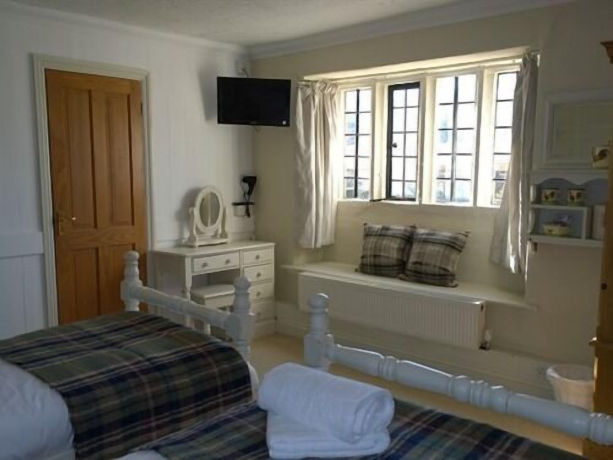 A bedroom with a bed, a dresser, a window with curtains, and a television on the wall.