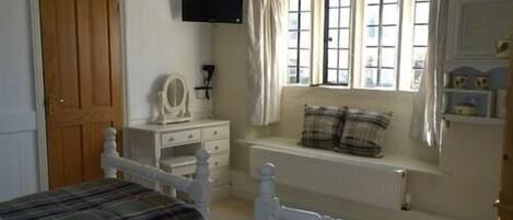 A bedroom with a bed, a dresser, a window with curtains, and a television on the wall.