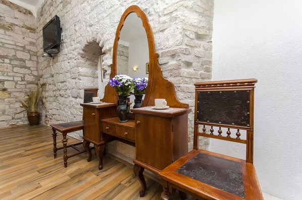 A room with a stone wall, wooden furniture, a mirror, and a vase with flowers.
