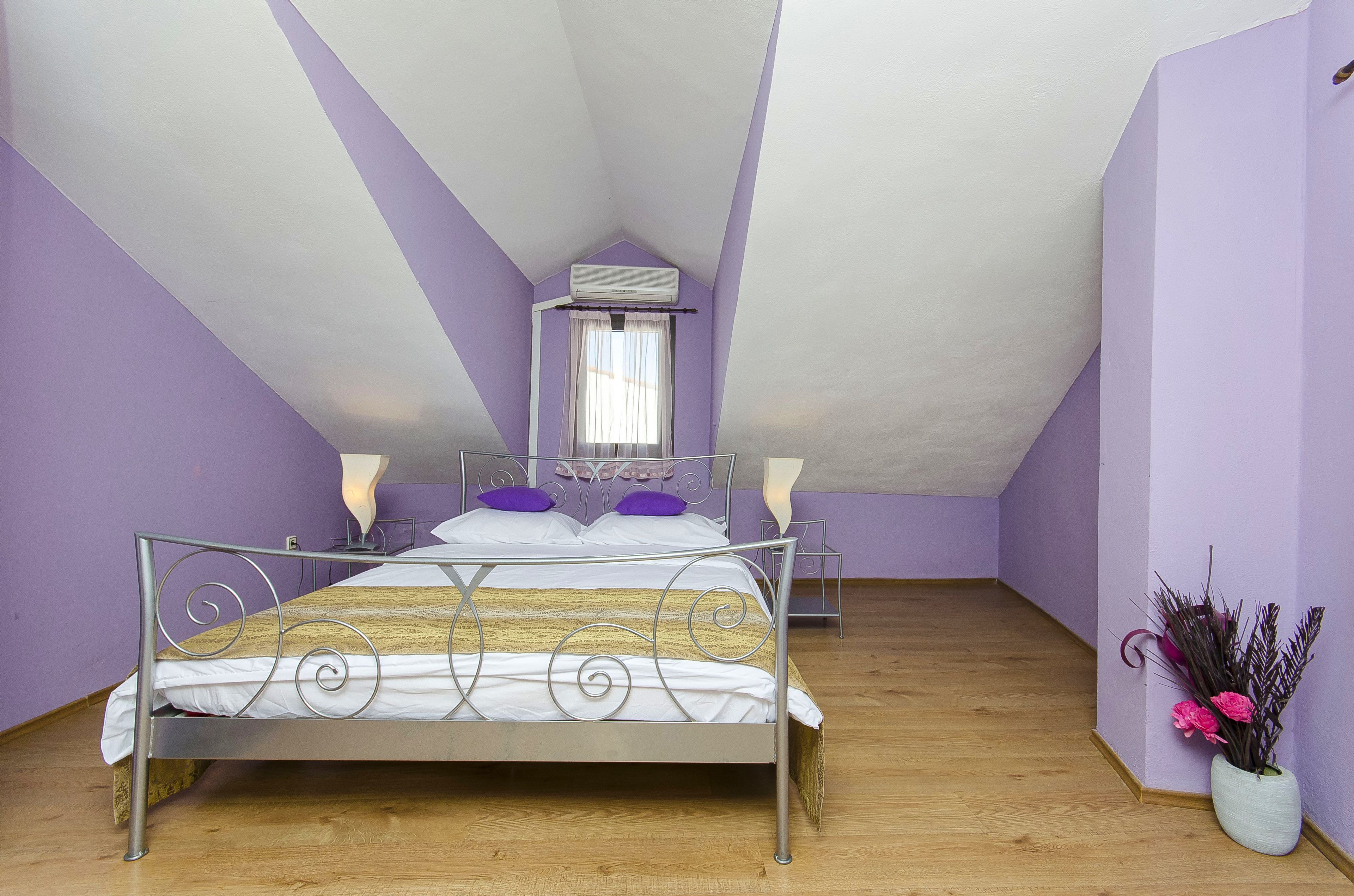 A bedroom with a sloped ceiling, a bed with a metal frame, a bedside table, a lamp, and a vase with flowers.