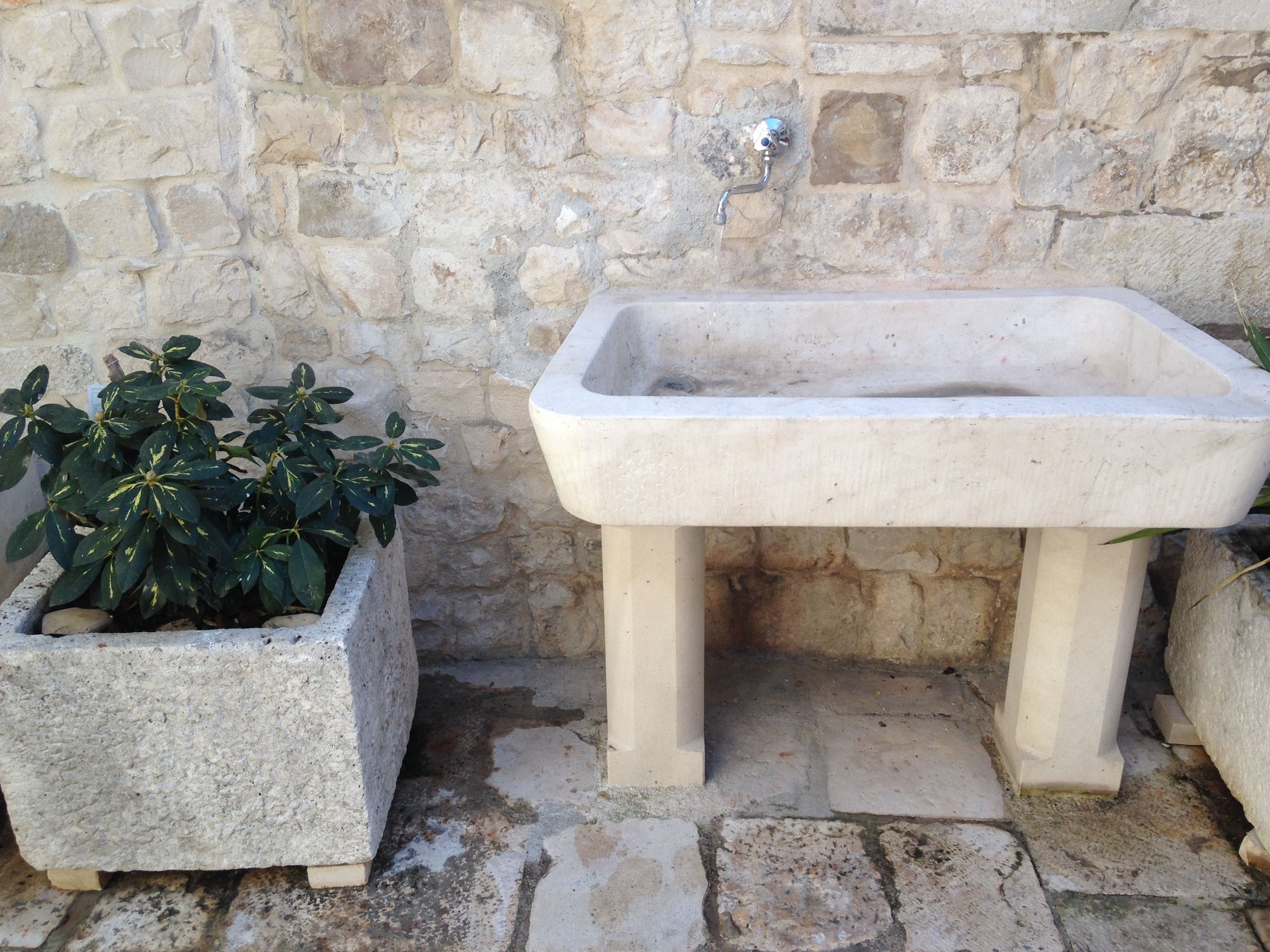A stone sink and planter against a stone wall.