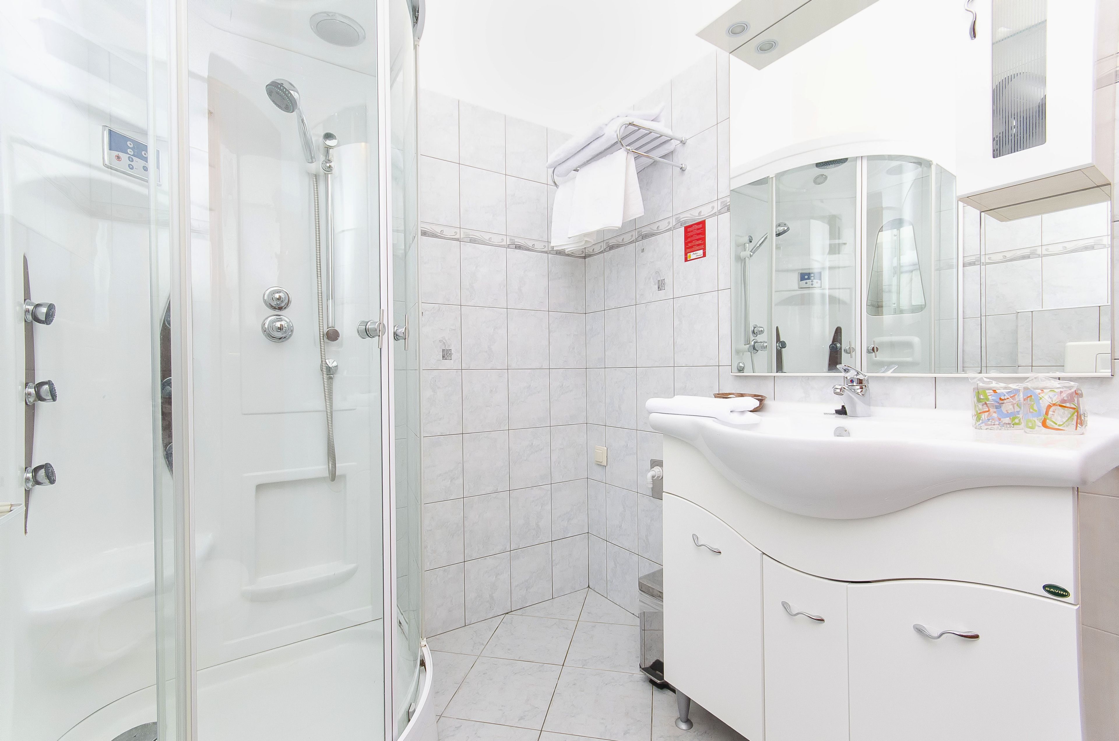 A modern bathroom with a glass-enclosed shower, white tiles, a vanity with a mirror, and a towel rack.