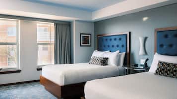 A hotel room with two beds, a large window, a framed picture, and a bedside table with a lamp.