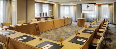 A conference room with a long table, chairs, and a projector screen displaying the hotel name.