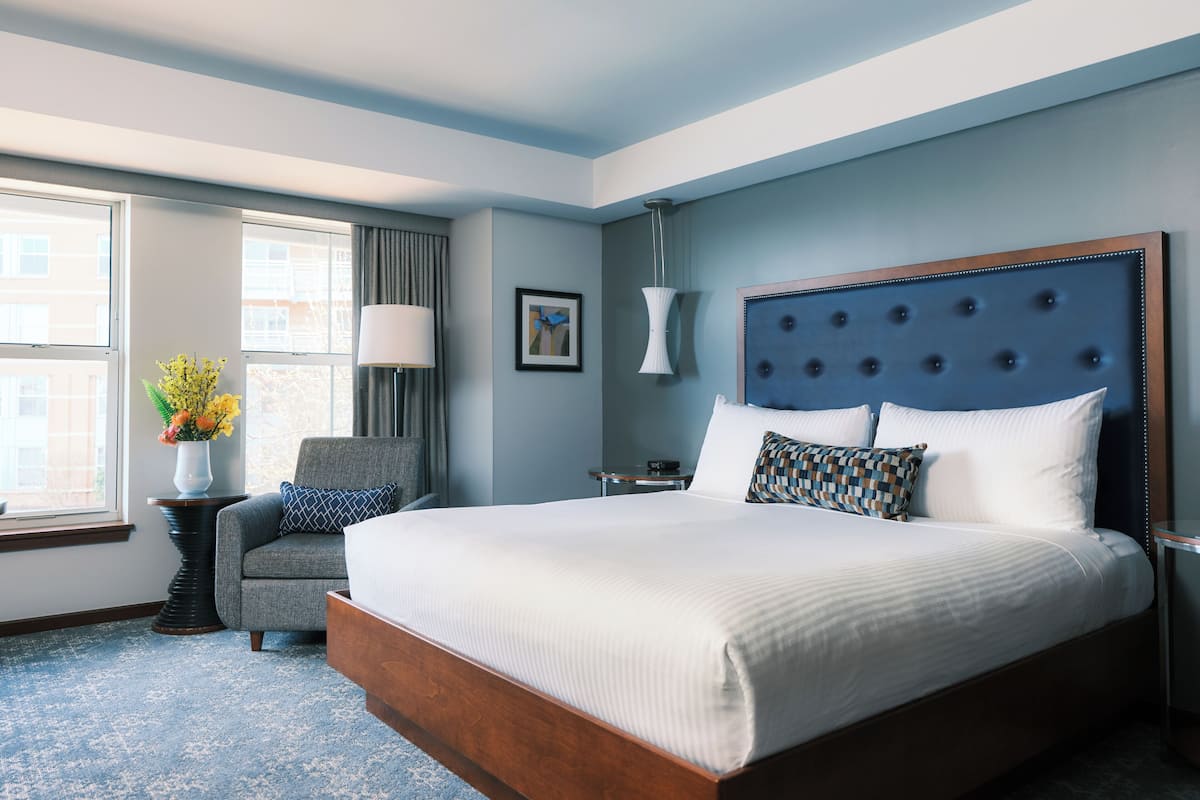 A hotel room with a large bed, a chair, a desk, and a window with curtains.