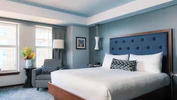 A hotel room with a large bed, a chair, a desk, and a window with curtains.