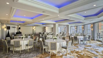 A spacious banquet hall with round tables, chairs, and a carpeted floor.
