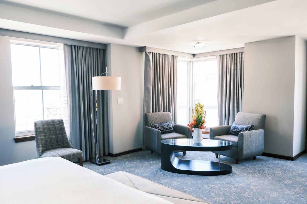 A hotel room with a bed, two armchairs, a coffee table, and a lamp.