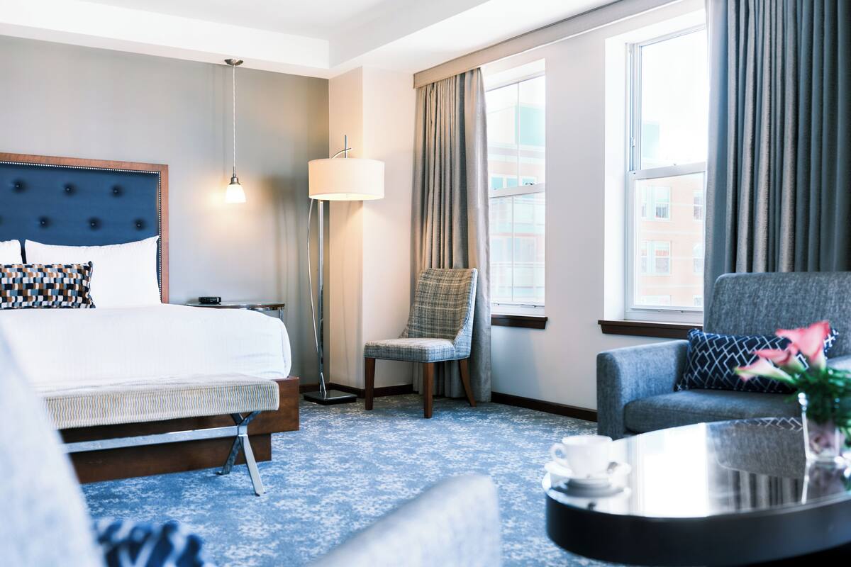 A hotel room with a bed, a chair, a sofa, a lamp, and a window with curtains.